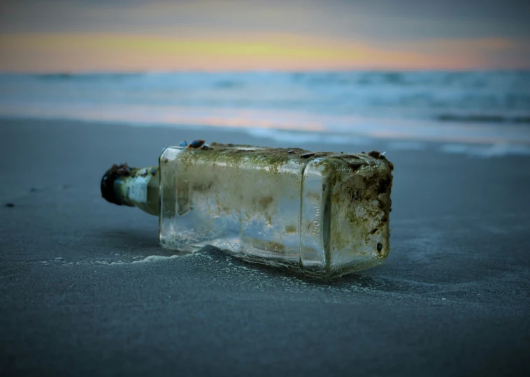 an empty bottle sitting on the beach with water coming out of it