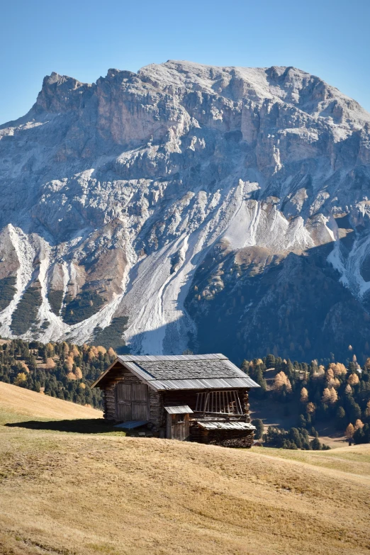 a cabin sits on a hillside in front of a snowy mountain range