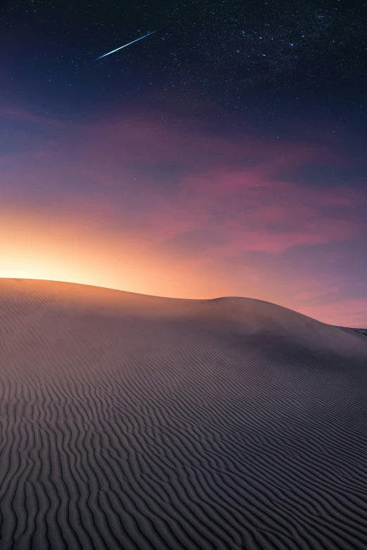 the sky and stars over sand dunes as the sun sets