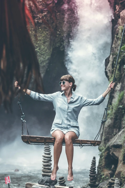 a woman in a white shirt and sunglasses sitting on a wooden swing