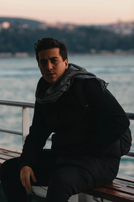 man with scarf on sitting on bench by the ocean