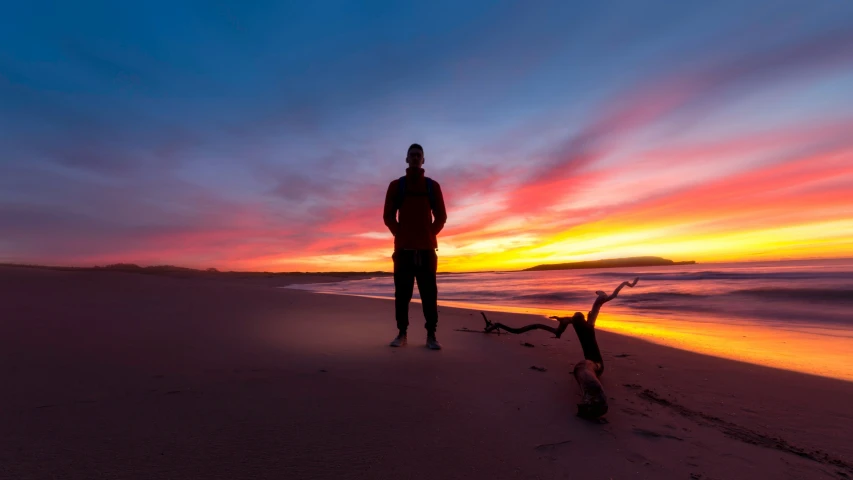 a man stands at the beach while watching the sun set