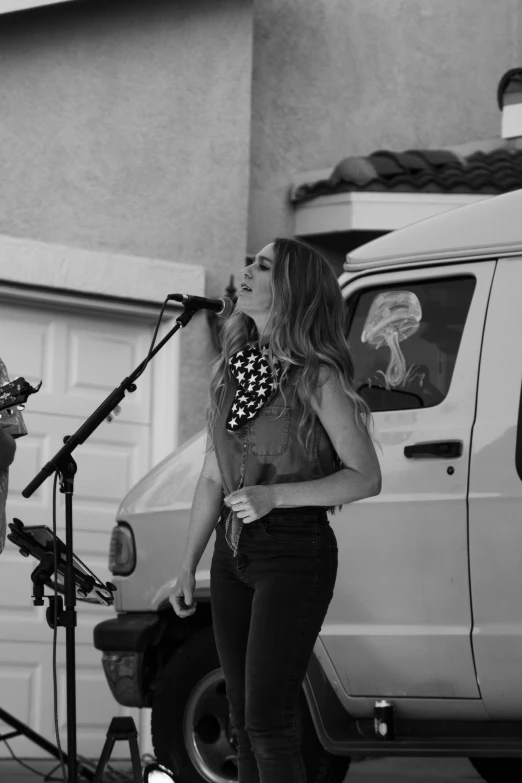 a young woman singing into a microphone while another sings in front of a car