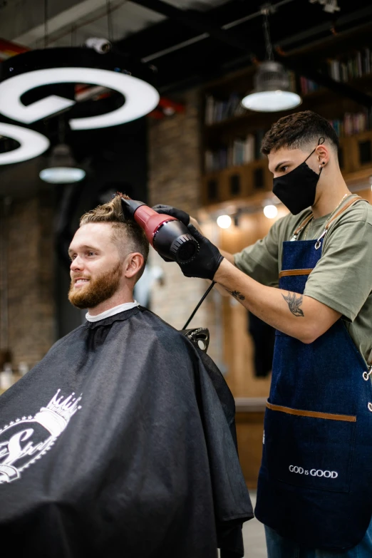 a barber with a beard wearing a mask and getting a haircut