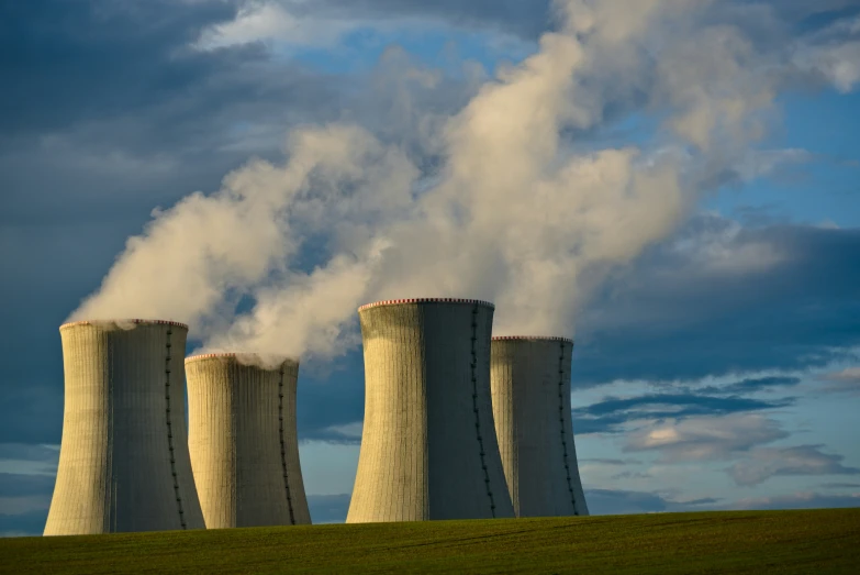 three cooling towers on a green hill with smoke coming out of them