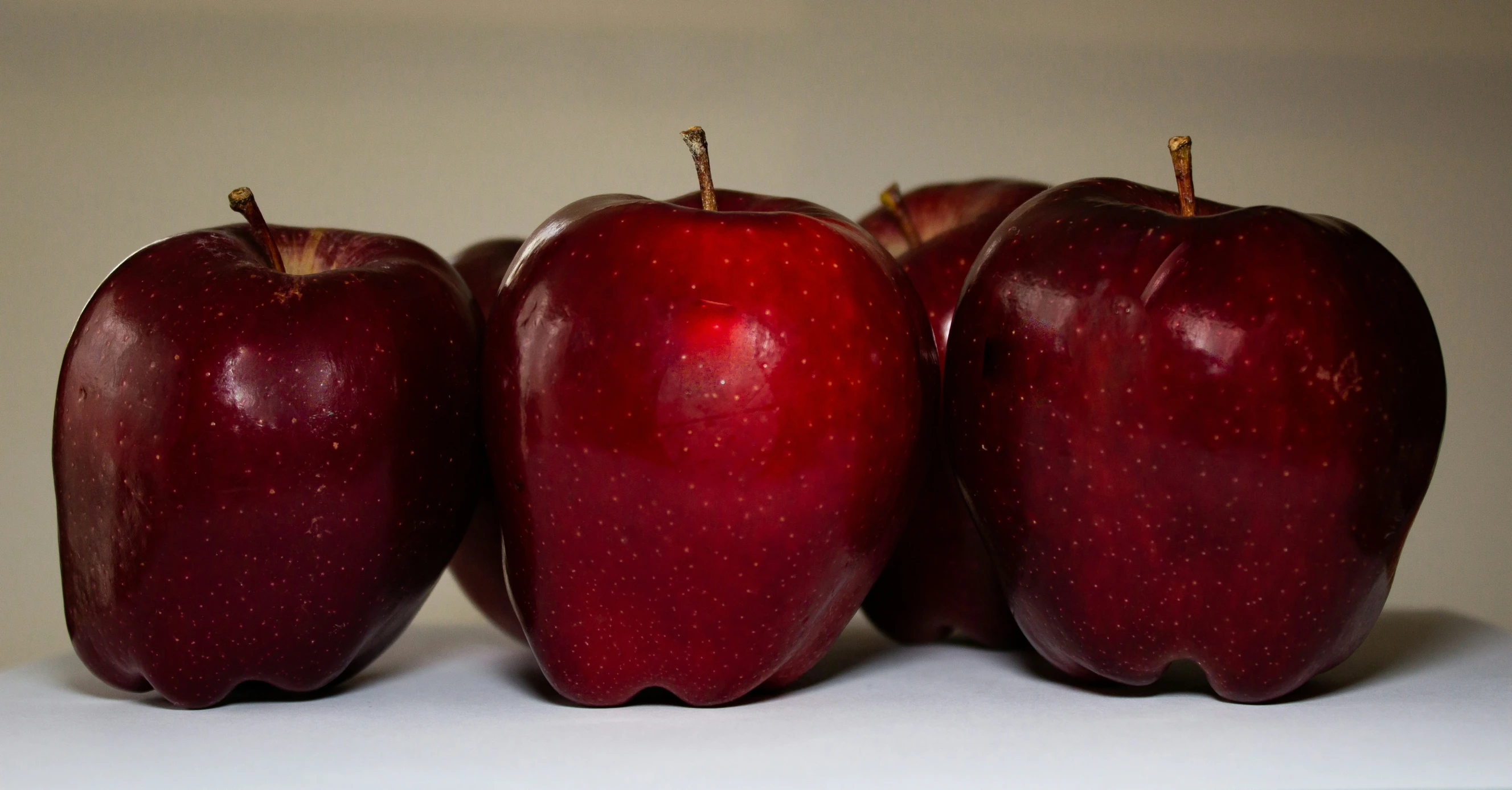 three red apples on white surface with reflection