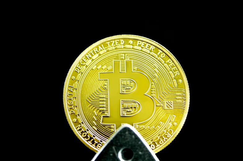 a bitcoin coin sitting on top of a tiny black piece of metal