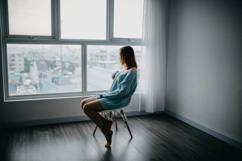 a woman sits by a window and stares at the city