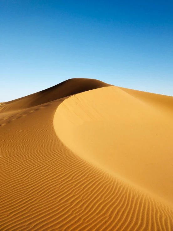 sand dunes with ripples in the distance under a blue sky