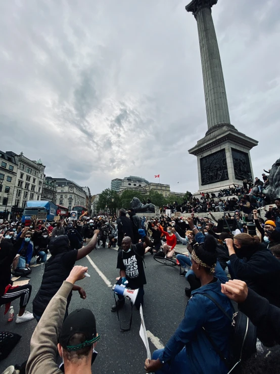 crowd of people on a city street with one person pointing at a tall monument