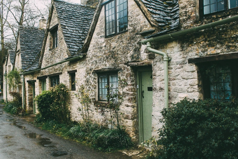 stone homes with green door and windows are all along the side of a road