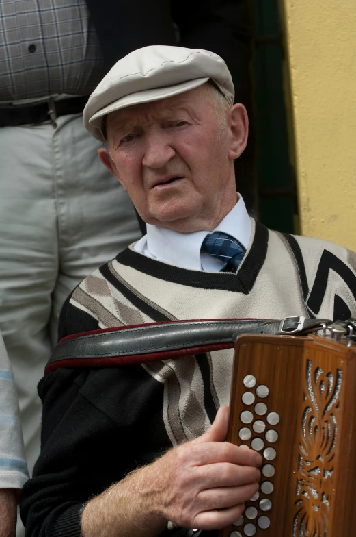 an old man is playing the accordion while holding a hat