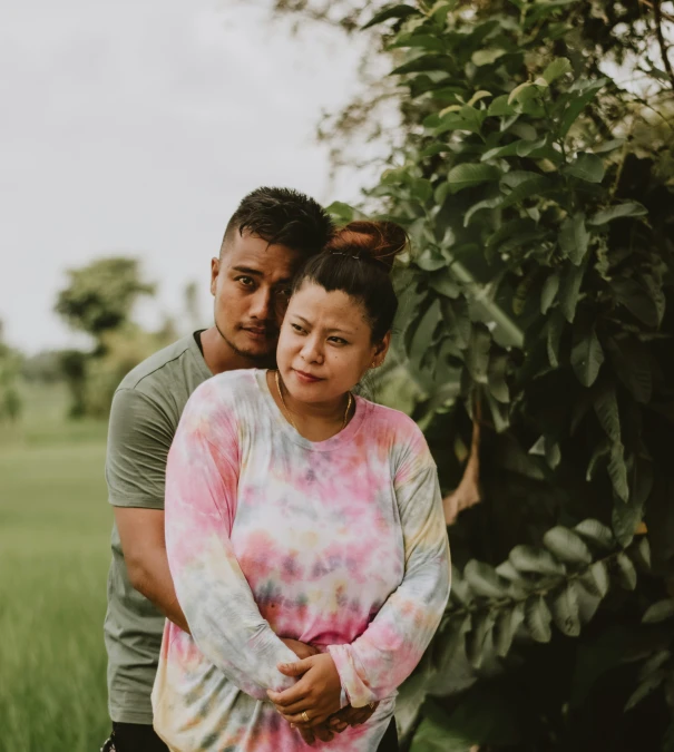 a couple poses for a po under a tree while in the middle of a field