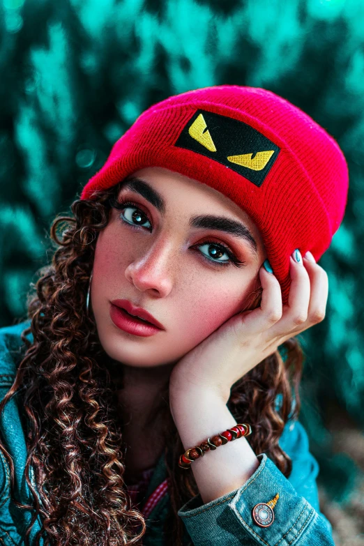 a woman sitting in front of trees and wearing a red beanie