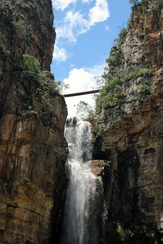 a waterfall with a bridge above it in the middle of some cliffs