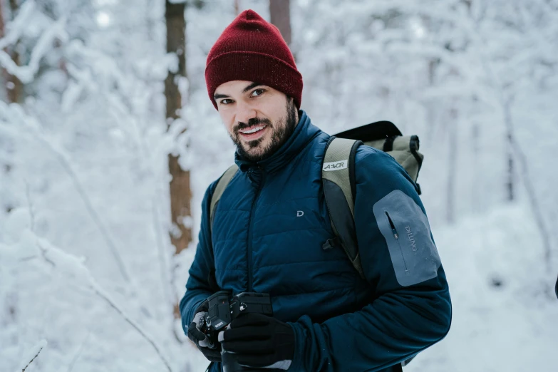 a smiling man standing in front of trees while wearing snow gear