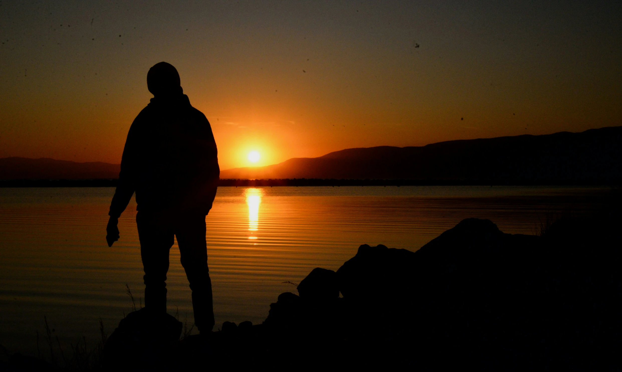 a person standing near the water with a sunset in the background