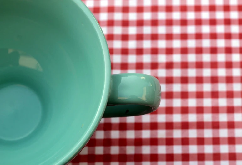 a green coffee cup sits in front of a red checked table cloth