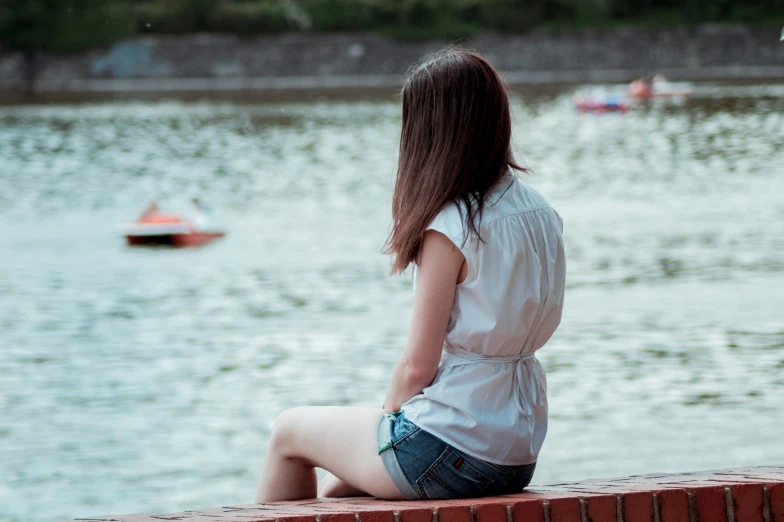 a young woman is sitting on a brick edge watching the water