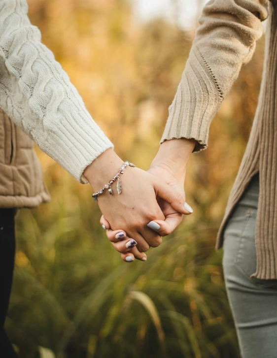 two people holding hands in a field with leaves