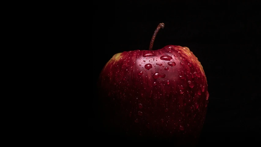 a wet red apple sitting next to black background