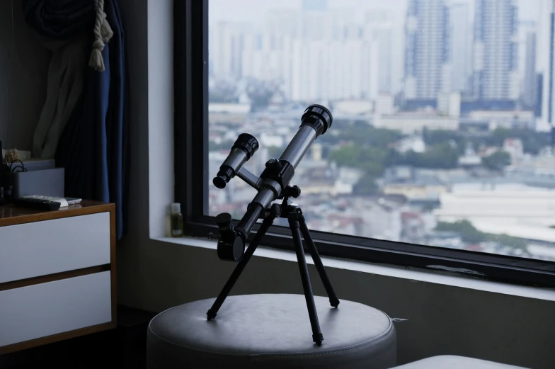 two telescopes on a tripod sitting in front of a window overlooking a city