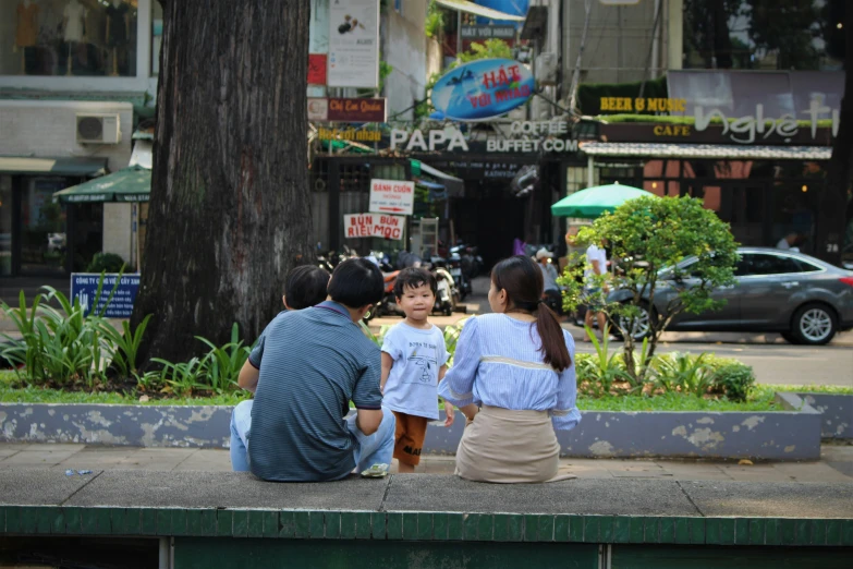 family sitting on bench next to tree outside city mall