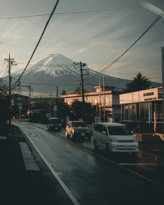 cars drive down a city street in front of a snow covered mountain