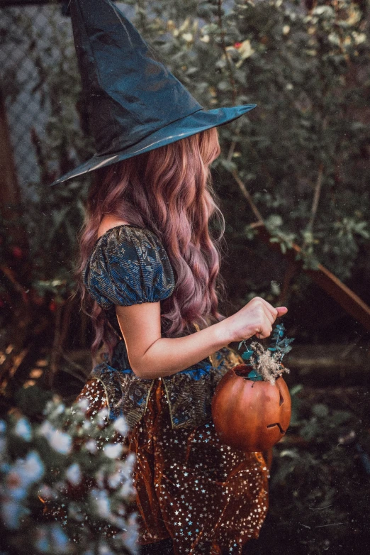 the girl is wearing a witch costume, hat and holding a pumpkin