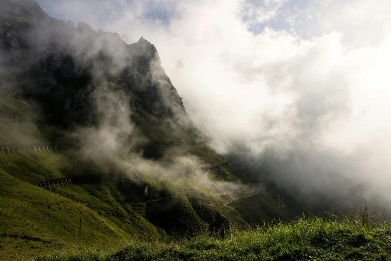 clouds hovering on a hill and grass surrounding it