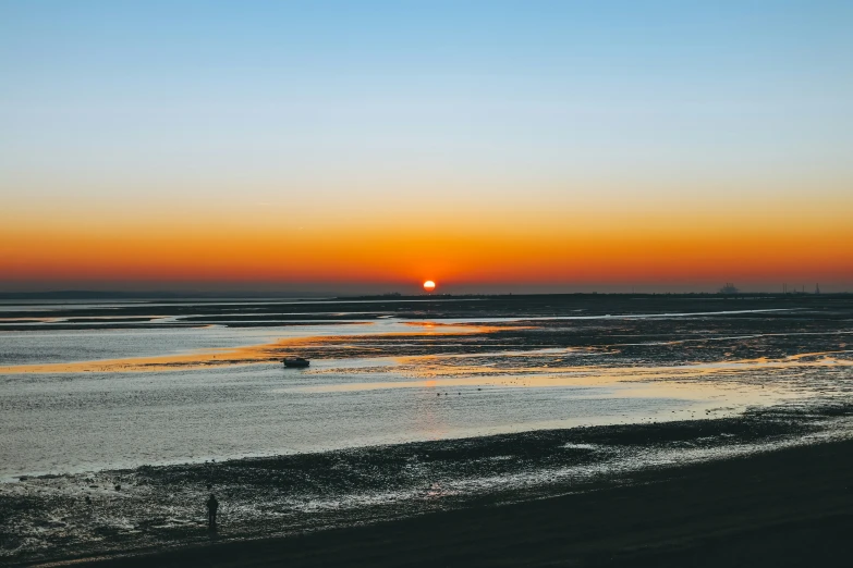 a sandy beach with the sun setting in the background