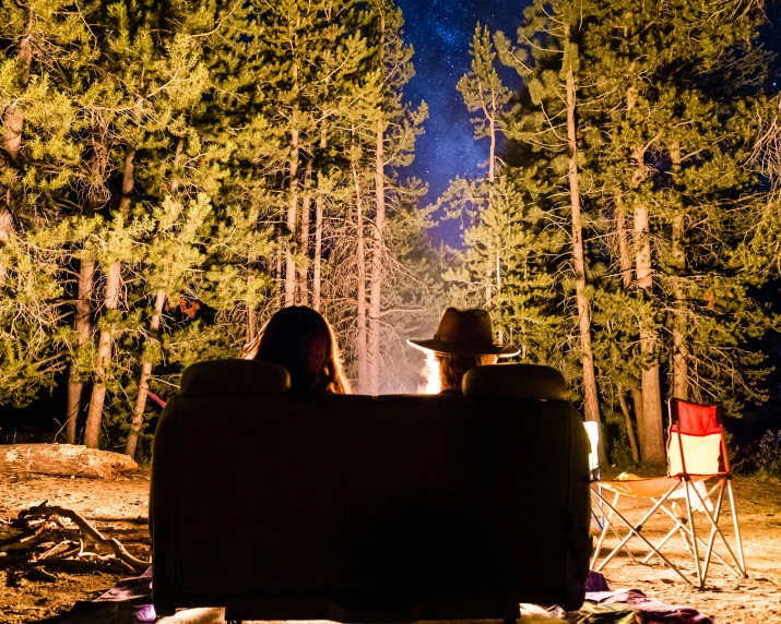 two people sit on a bench next to a campfire