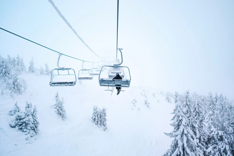 a person riding on a ski lift with snow covered trees