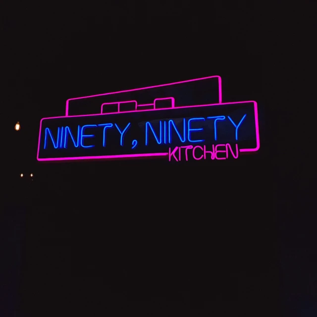 the neon sign for ninety ninety kitchen on the corner of a street
