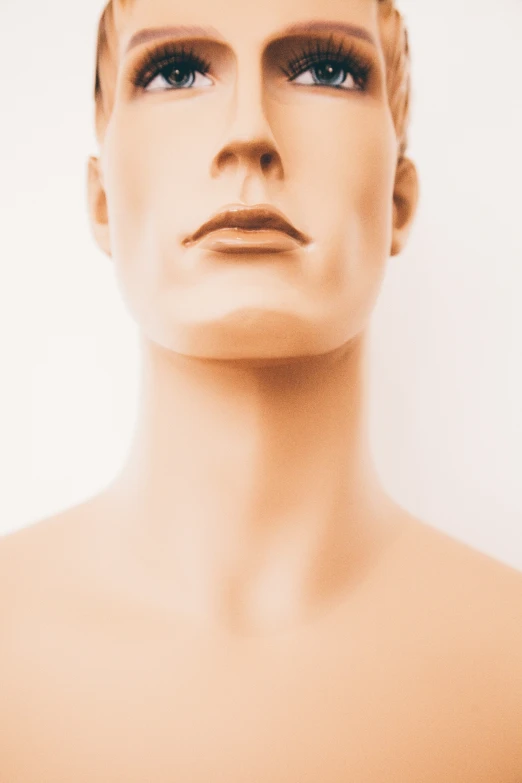 a mannequin head standing next to white wall