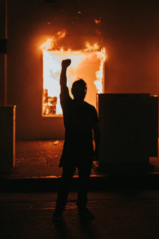 a man is standing on the street at night in front of a fire with flames burning through the windows