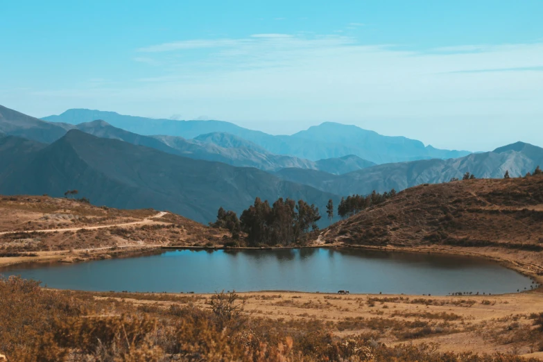 large lake in the middle of a field with mountains and blue sky