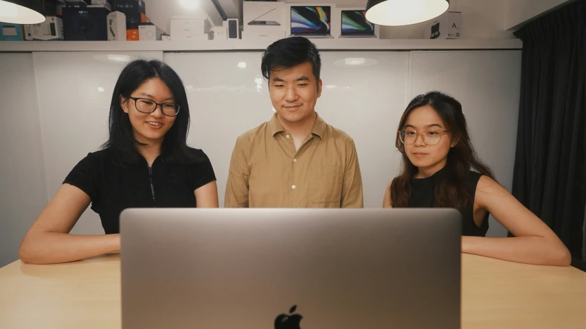 three people posing for a po behind a laptop computer