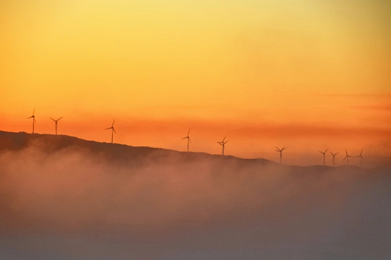 the sun rising over some hills and windmills