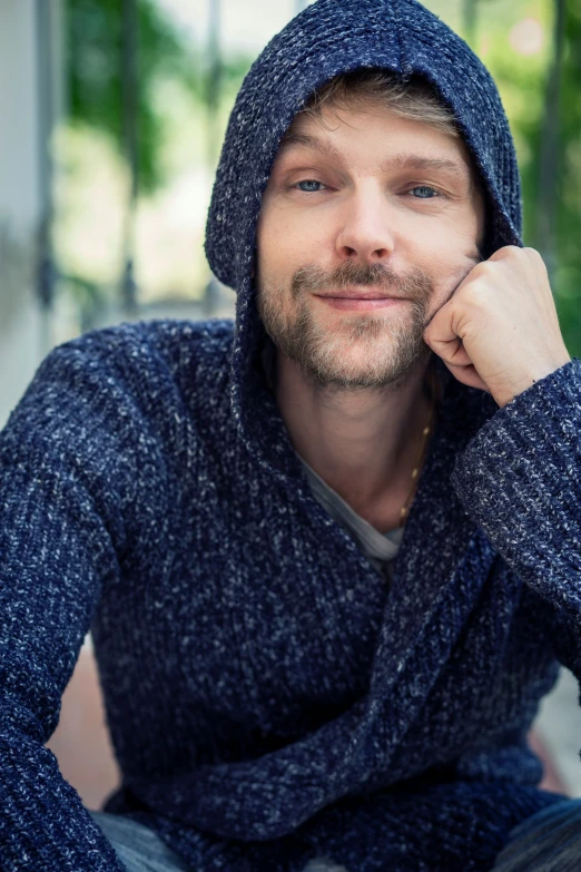 the man is posing for a picture, wearing a blue hoodie