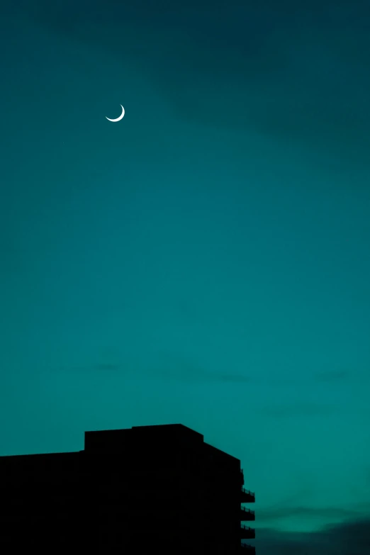 the sky above a tall building with a crescent above