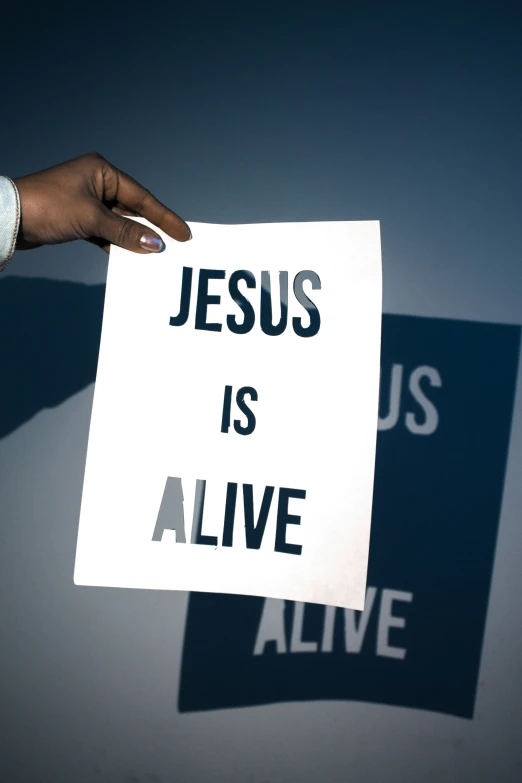 a person is holding a white paper with jesus is alive on it