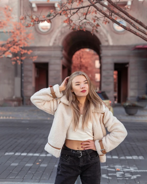 a young woman stands on the sidewalk while wearing black pants and a beige jacket