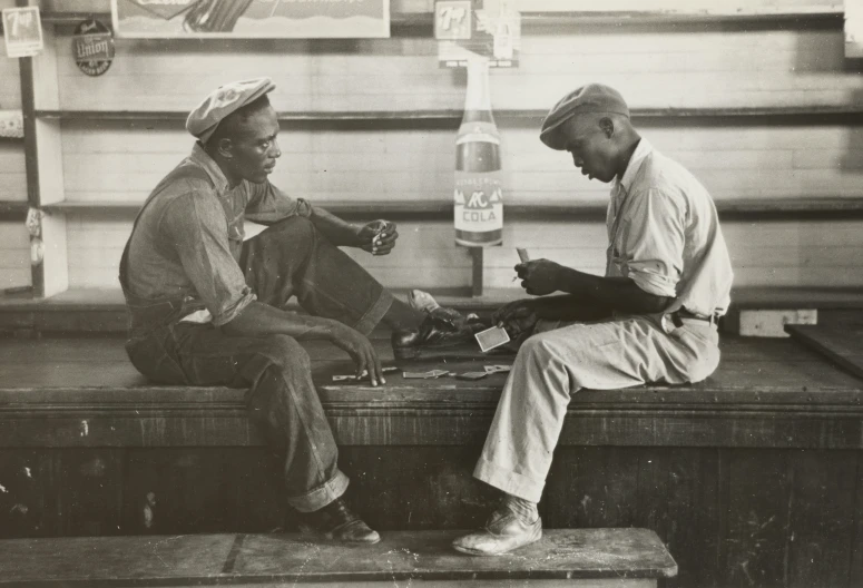 two men sitting on a bench, each drinking a beer