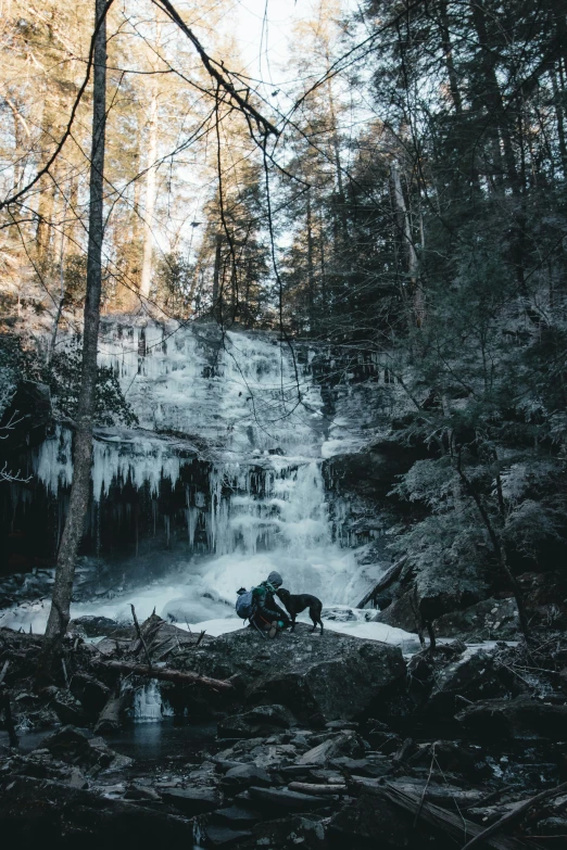 people camping on the bank of a river next to some frozen waterfall