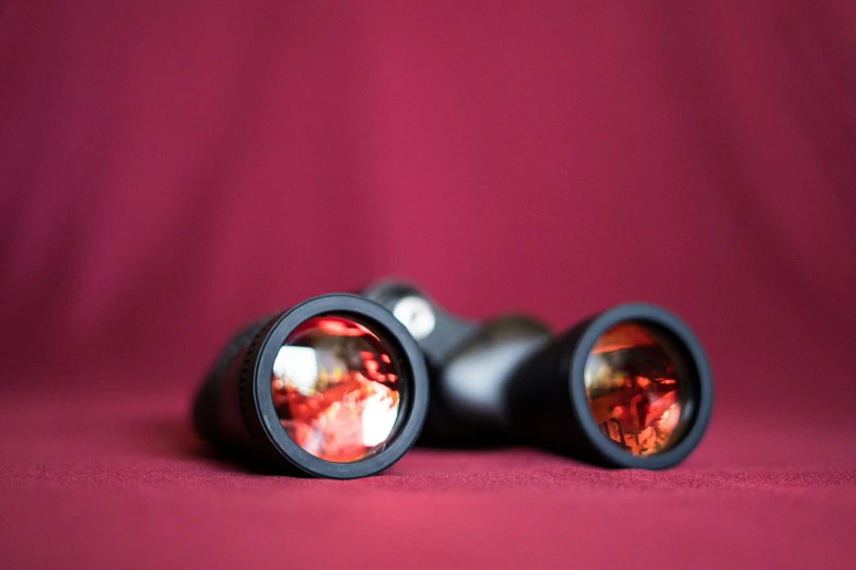 two binoculars on a burgundy background showing reflection