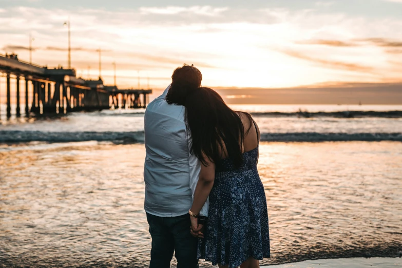 a man and woman are standing at the beach at sunset