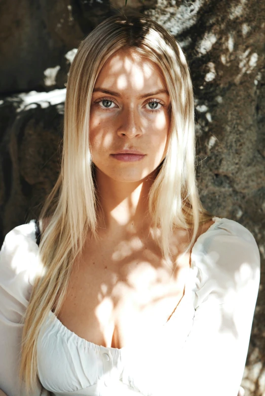 a very beautiful blonde wearing a white top standing by a tree