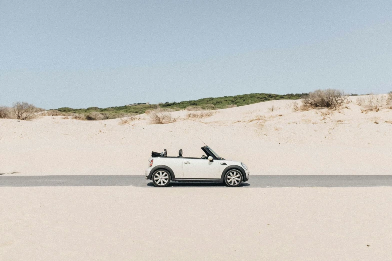 white convertible car driving along a sandy shore