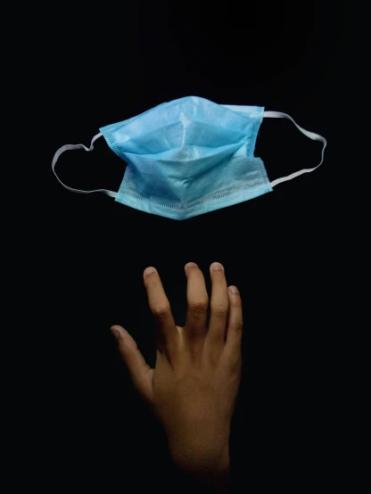 a hand wearing a surgical face mask on a black background
